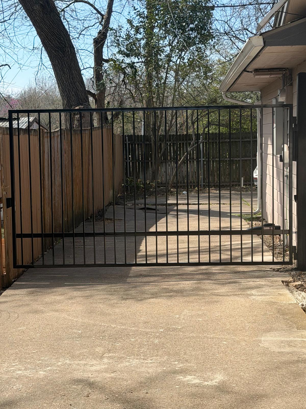 Iron swing gate open across a concrete driveway beside a Dallas home