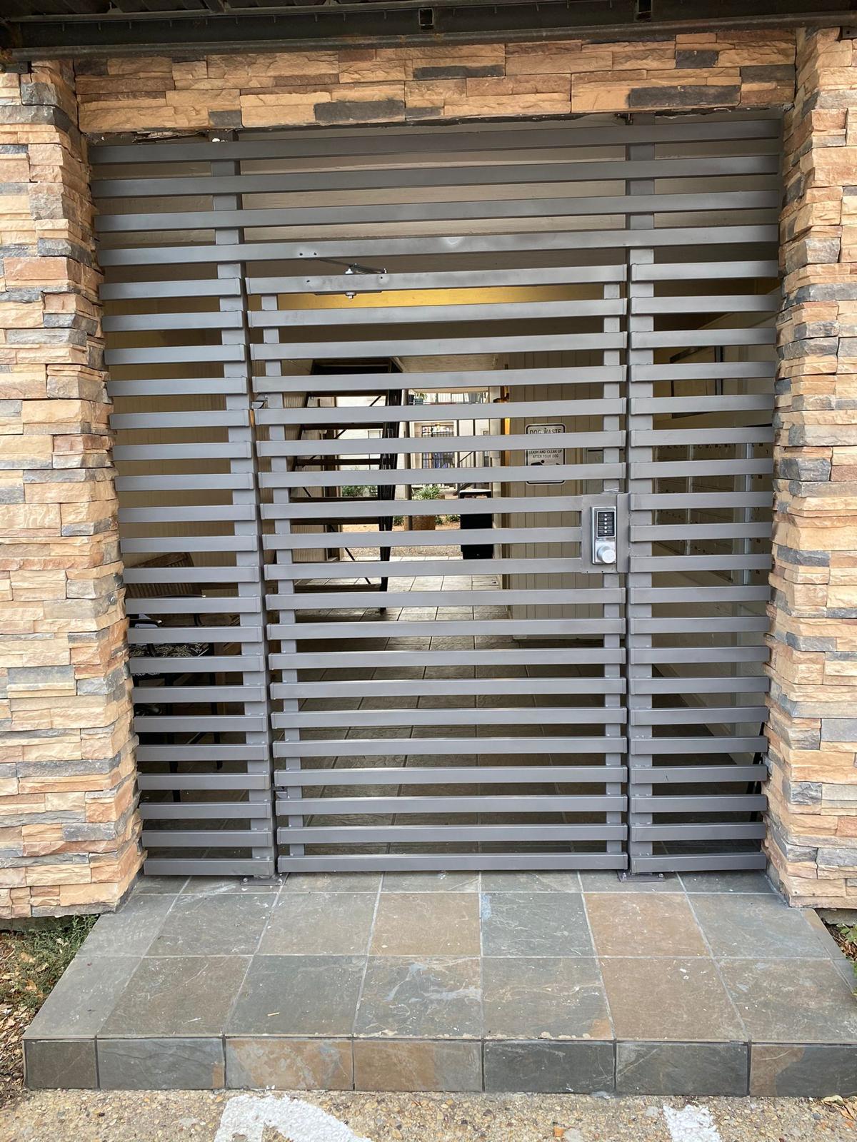 Horizontal slat steel pedestrian gate set into a stone masonry opening in Dallas