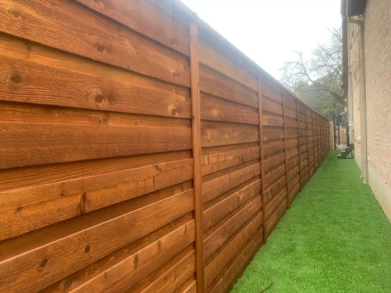 Tall horizontal board-on-board cedar fence stained along a Dallas property line