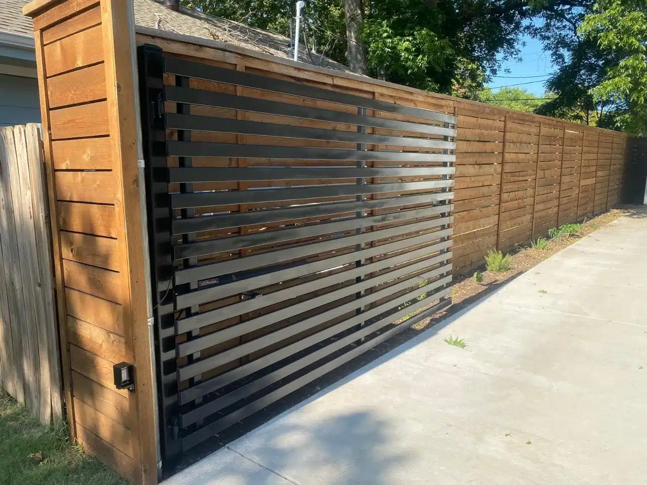 Modern horizontal slat iron swing gate beside a cedar fence in DFW
