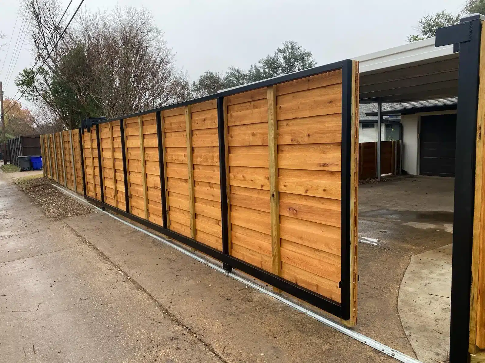 Horizontal wood sliding gate with black metal framing beside a concrete driveway in McKinney