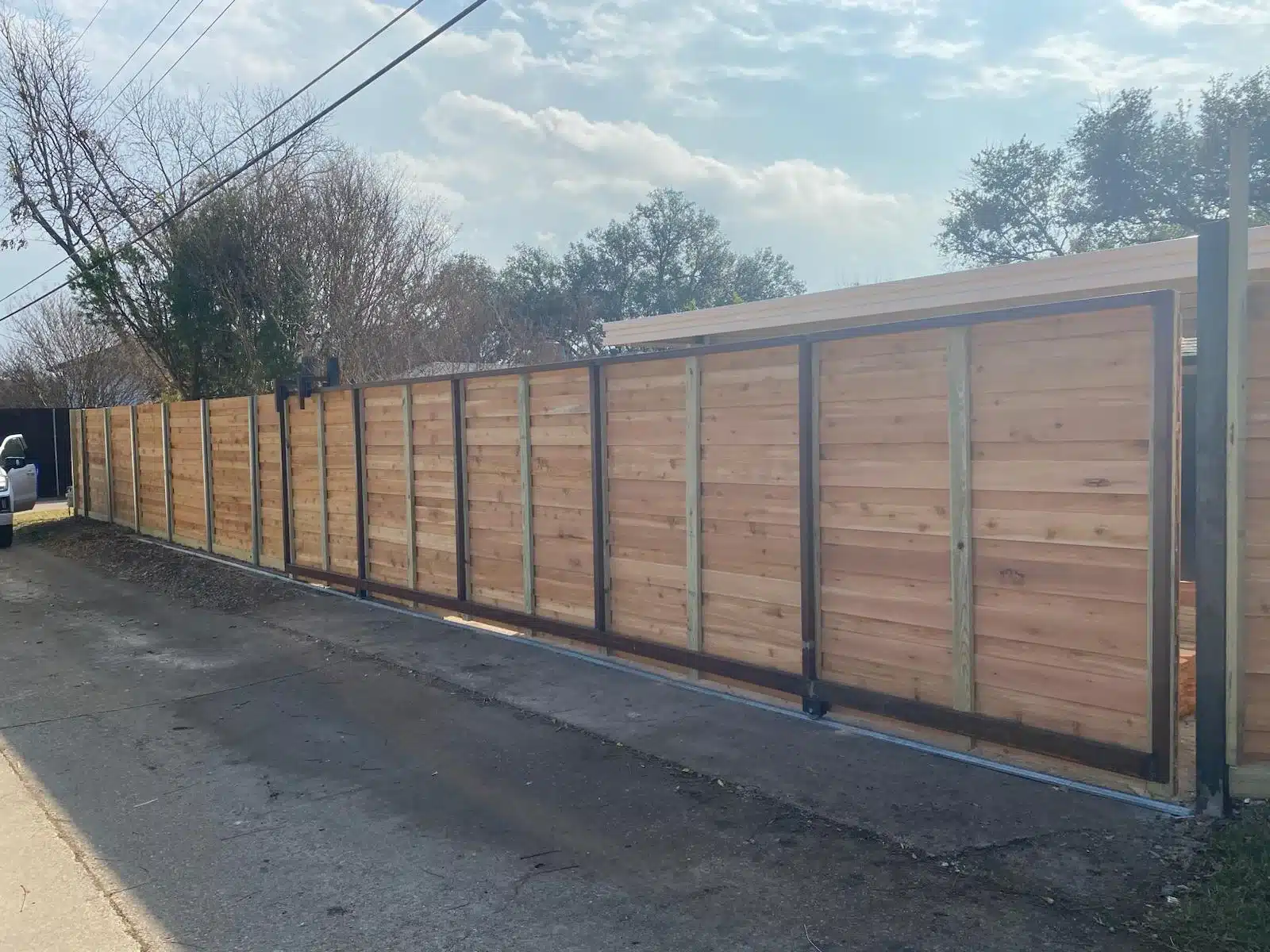 Horizontal wood driveway gate with dark metal framing and a track beneath the bottom rail