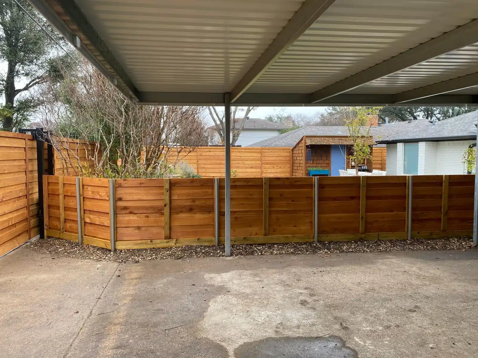 Horizontal wood fence panels with metal support posts beneath a corrugated patio cover