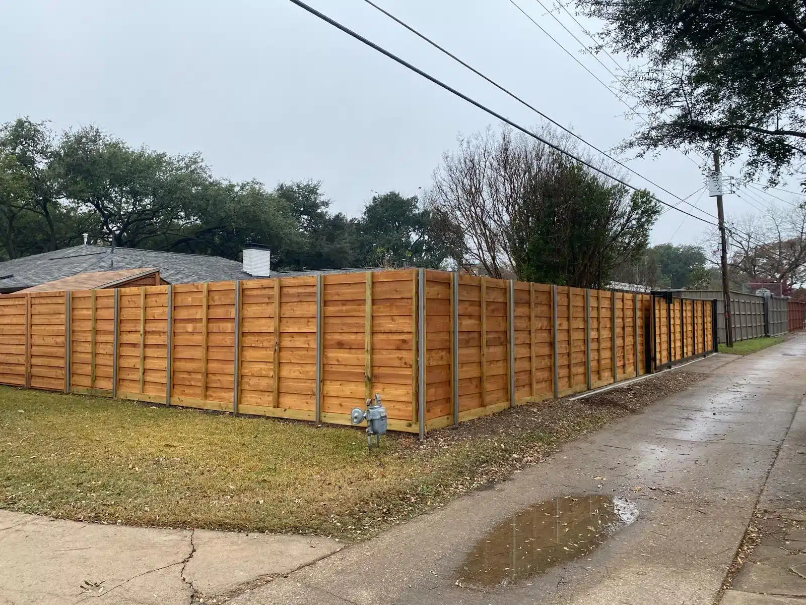 Horizontal wood privacy fence with visible metal posts wrapping a corner beside a paved residential lane.