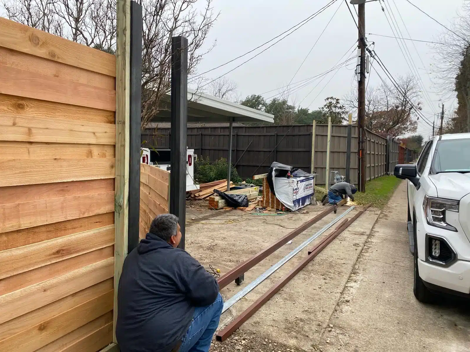 Horizontal wood gate area with black steel posts, metal framing on the driveway, and workers nearby.