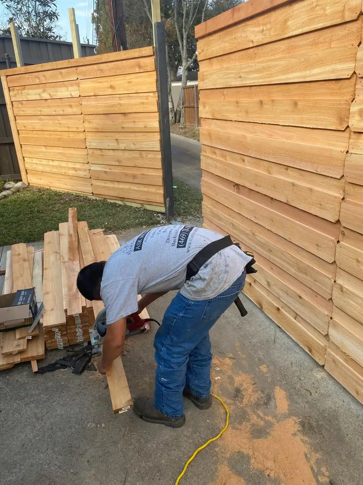 Worker cutting a wood board beside horizontal fence panels during installation