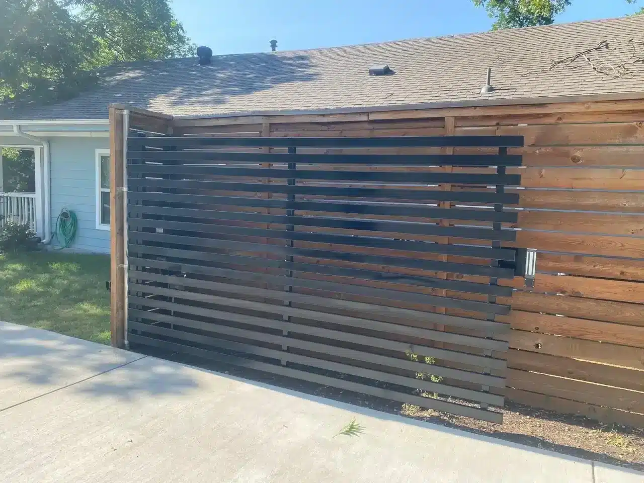 Horizontal black and wood slat privacy fence along a residential driveway
