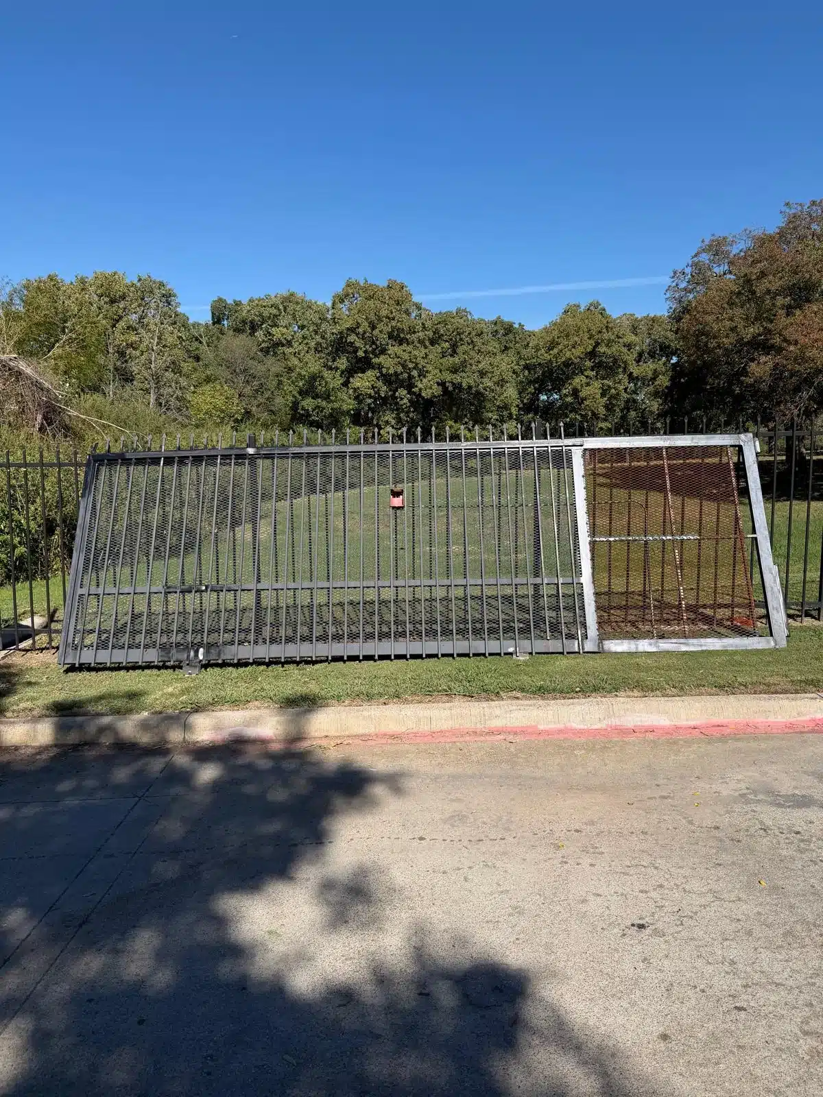 Wide mesh-panel driveway gate with a framed pedestrian section against a backdrop of trees.