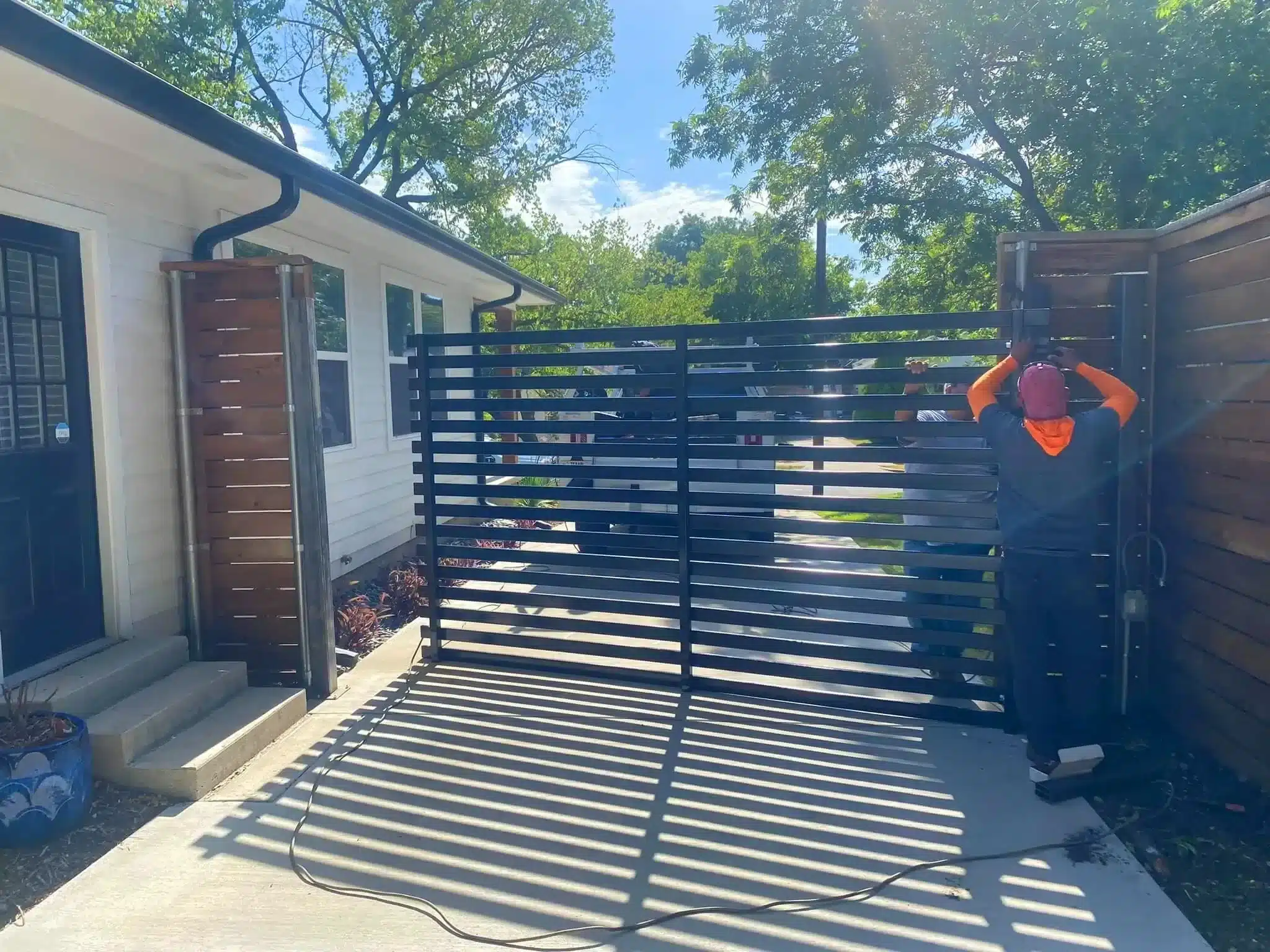 Black horizontal slat metal gate open on concrete driveway between pillars.