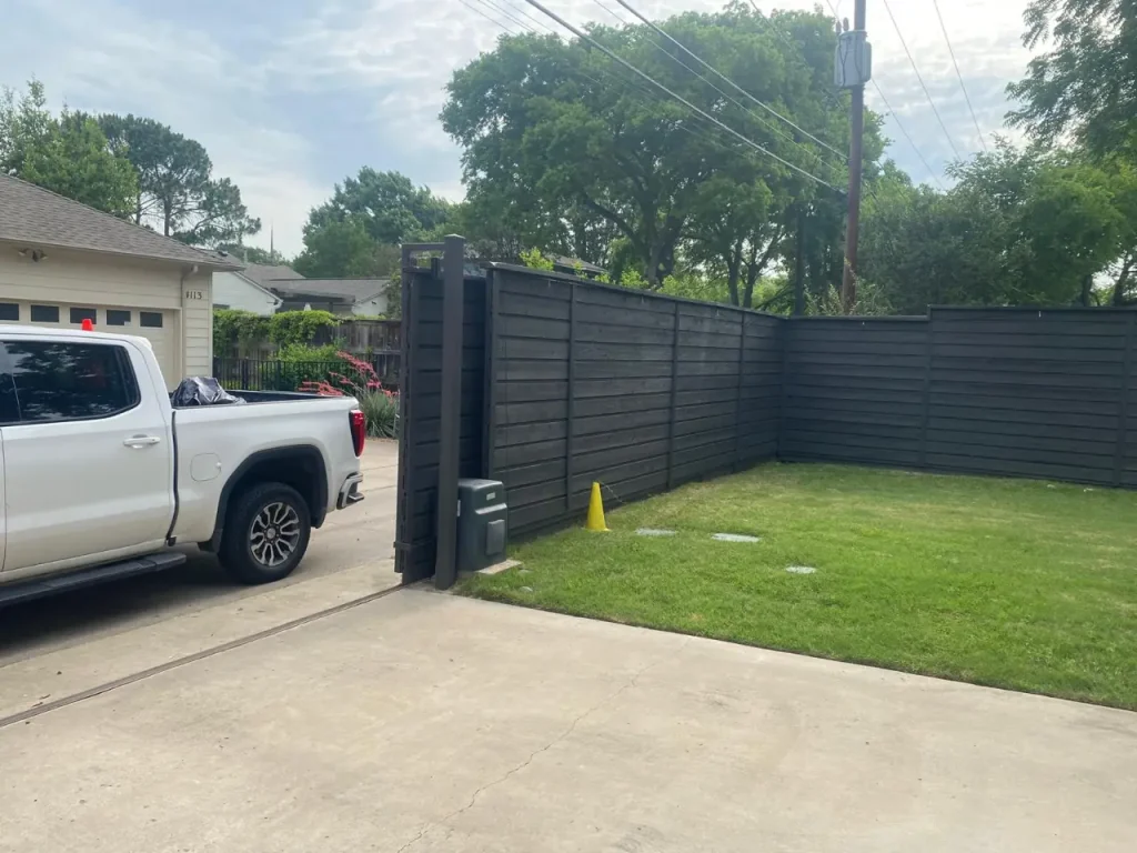 Automatic black sliding driveway gate opening beside a white pickup truck in a residential driveway.