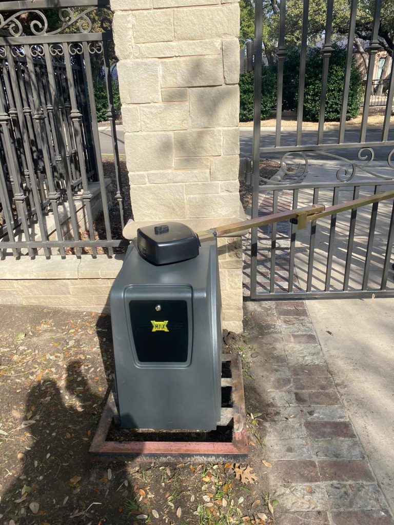 Automatic gate opener installed beside an iron gate and stone pillar on a residential driveway.