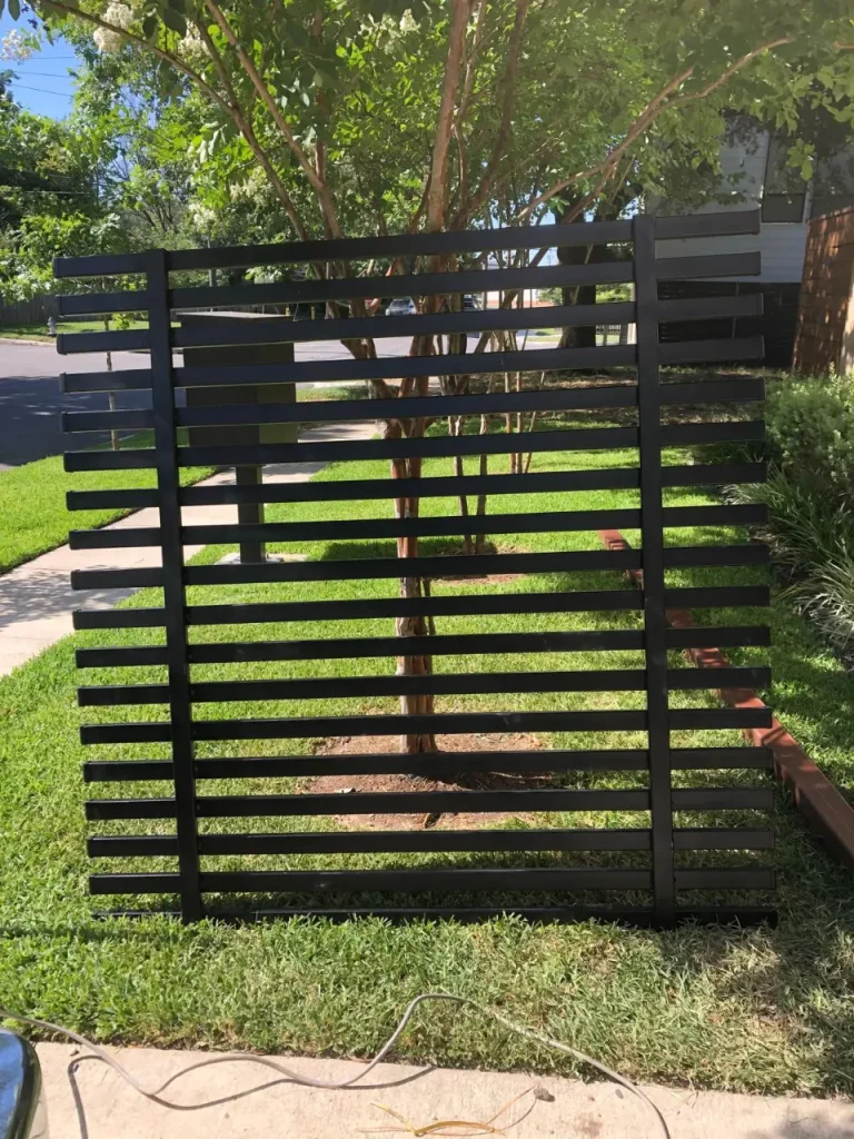 Black horizontal aluminum gate installed along a residential sidewalk with landscaped lawn.