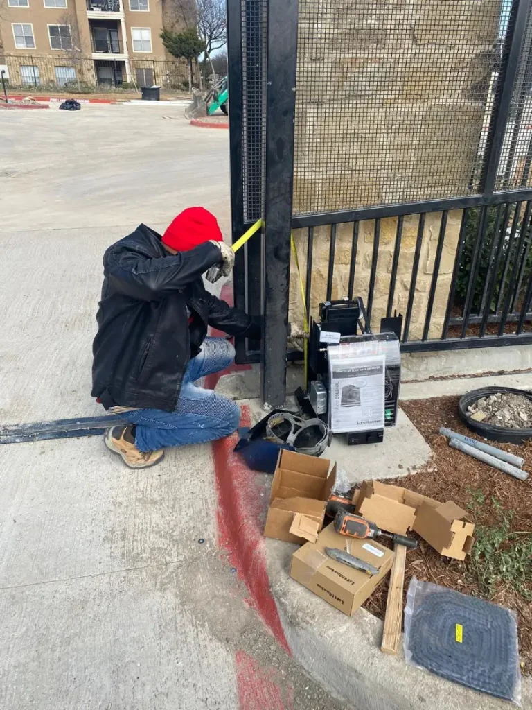 Worker measuring a metal gate post with tools on the ground during gates and openers installation.