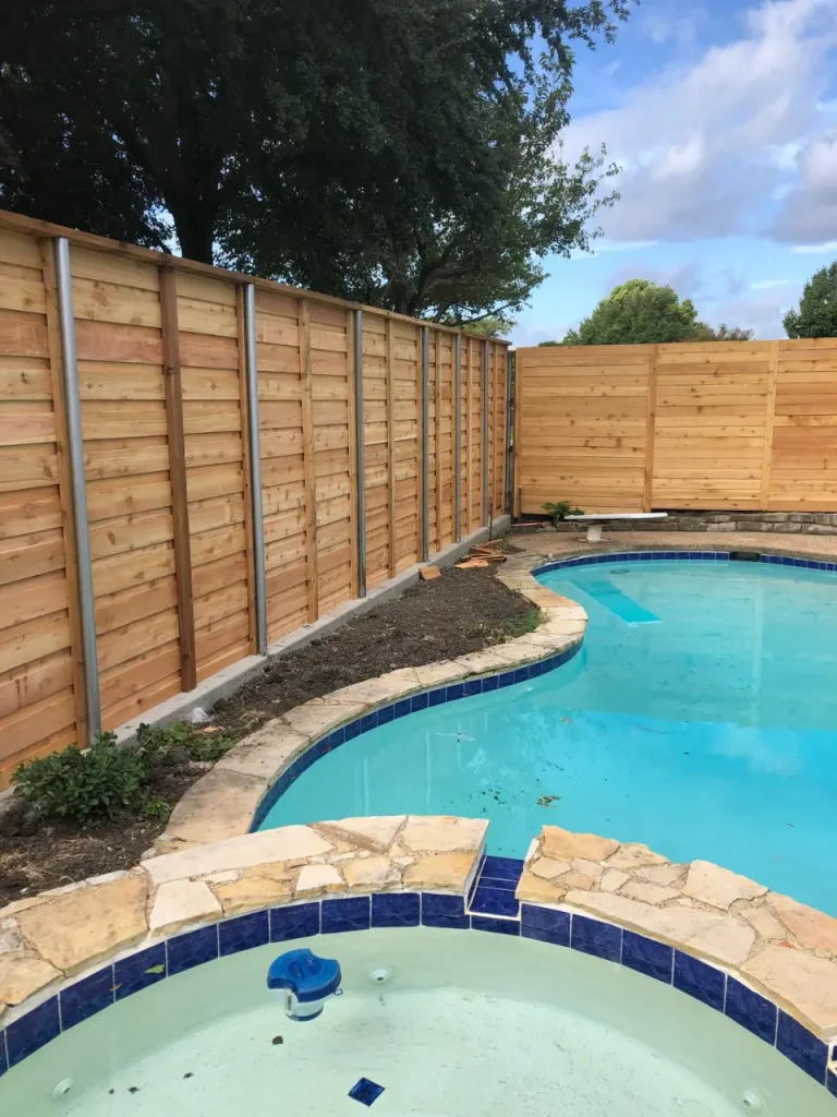 Wooden pool fence running along the edge of an in-ground swimming pool, providing privacy and safety enclosure.