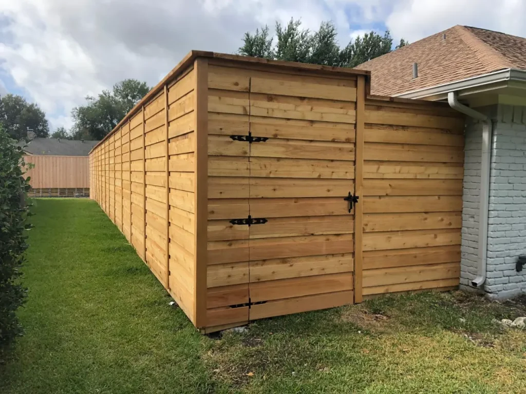 Tall wooden pool fence with double gate installed along a backyard lawn beside a residential home.